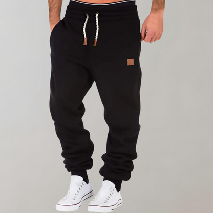 Black joggers worn by a model with white trainers, hand in pocket, braided drawstring 1