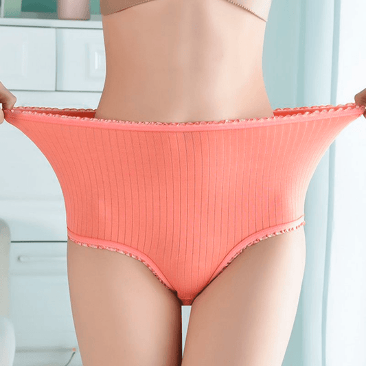 Model stretching the waistband of coral ribbed high-waisted briefs wide to show how elastic the frilled edging is. 1