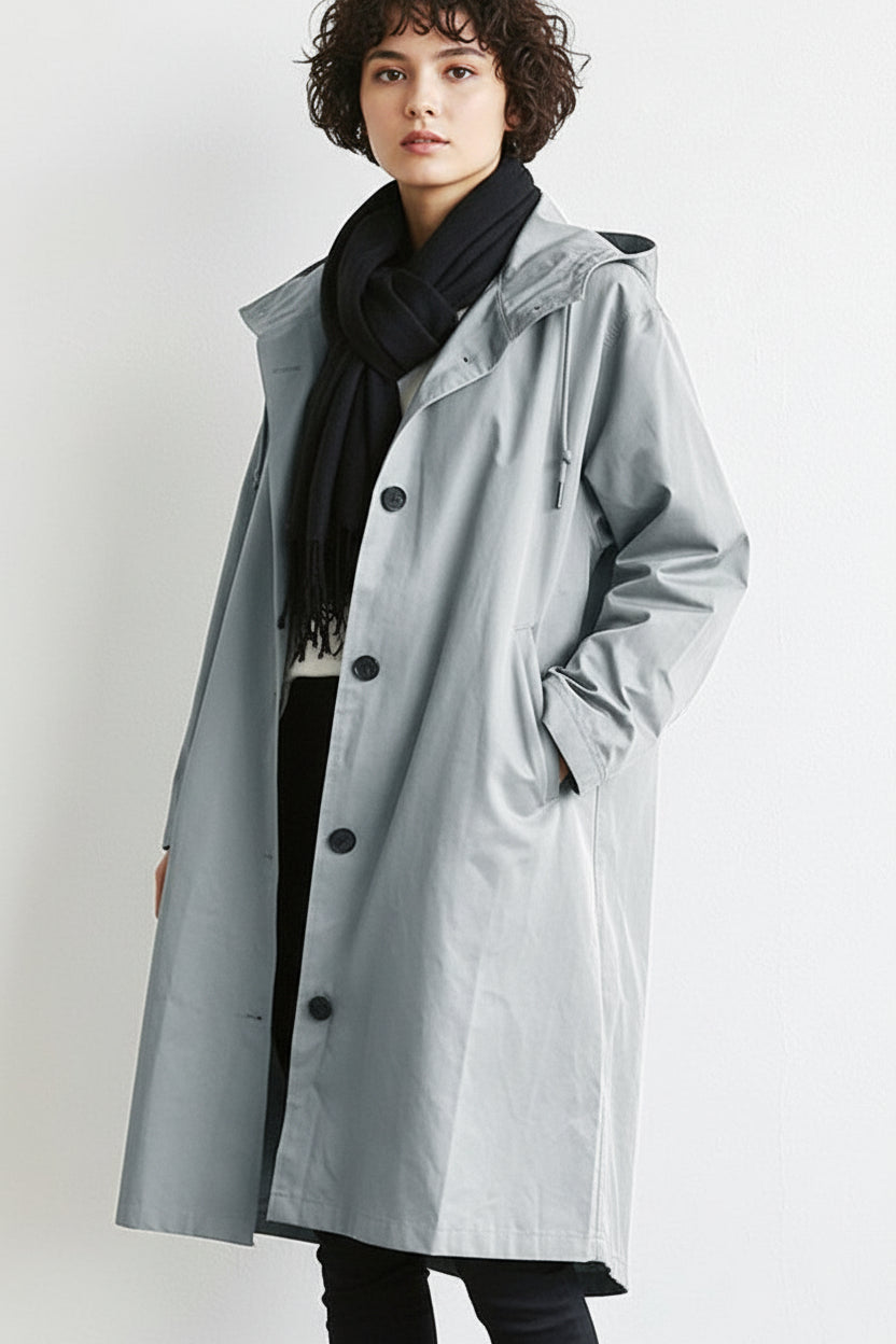 Model in a pale grey hooded button-up coat with a black scarf, one hand in pocket 1