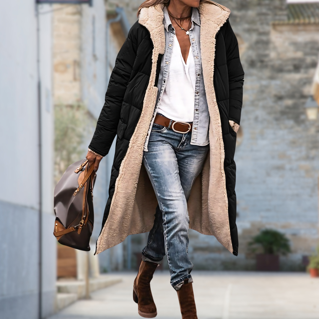 Woman walking along a street in the long black quilted coat, worn open to show the cream fleece lining. 4