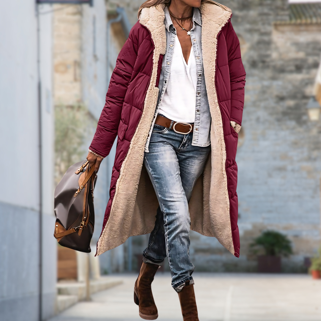 Woman walking outdoors in the long burgundy quilted coat, open to show the cream fleece lining and fleece-lined pocket. 6