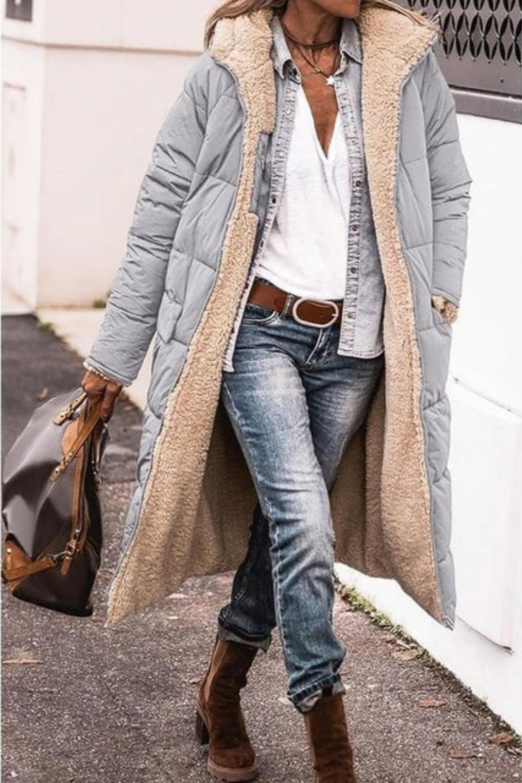 Woman walking past a white wall in the long light grey quilted coat, open to show the cream fleece lining. 8