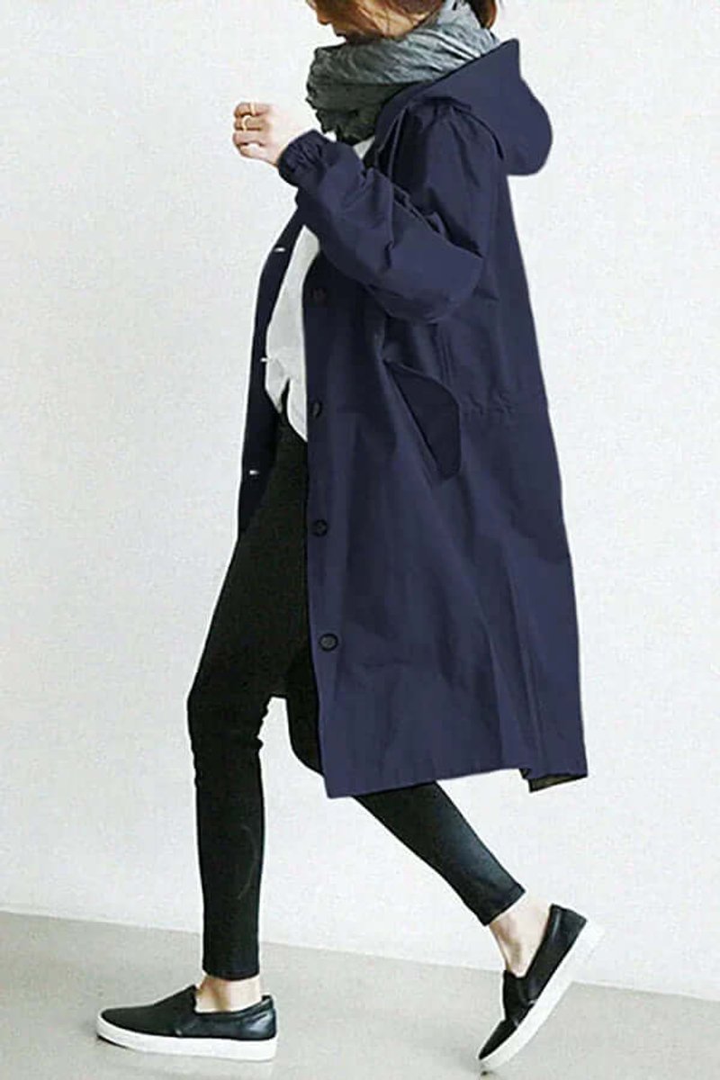 Side view of the navy coat on a walking model, showing the hood, pocket and button front 8