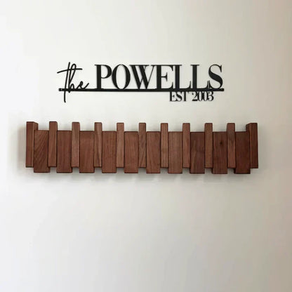 Dark wood rack with hooks folded flat, mounted on a white wall beneath a black name sign 6