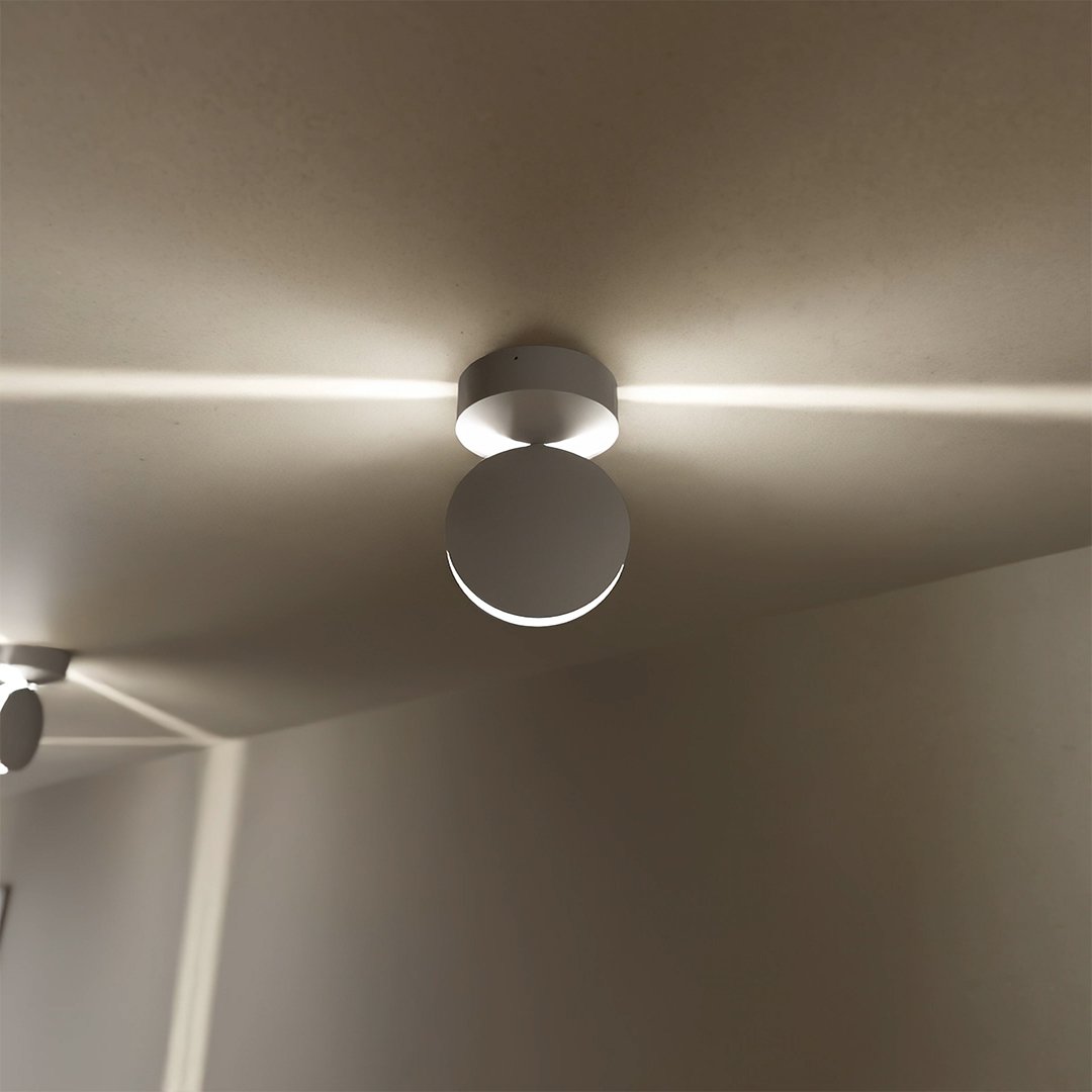 Close view of a white ceiling-mounted light with a round angled head, projecting a horizontal beam of light across the ceiling. 3