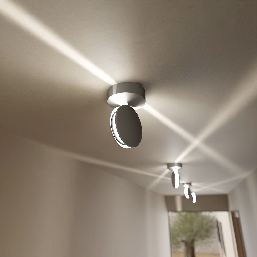 White ceiling light with its round head turned sideways, casting crossing diagonal beams across the ceiling of a hallway. 4